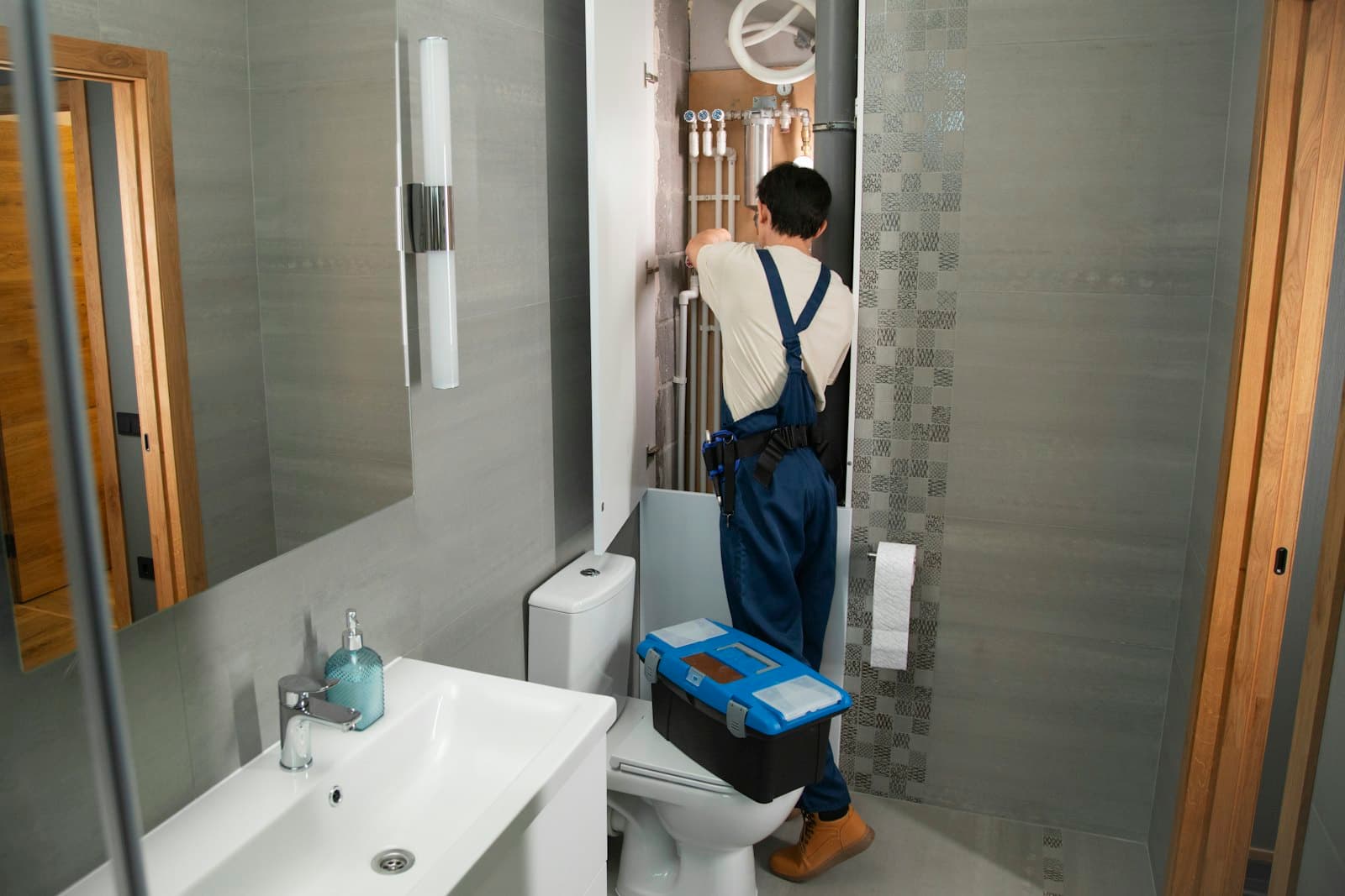 A plumber working on pipework behind a bathroom wall panel