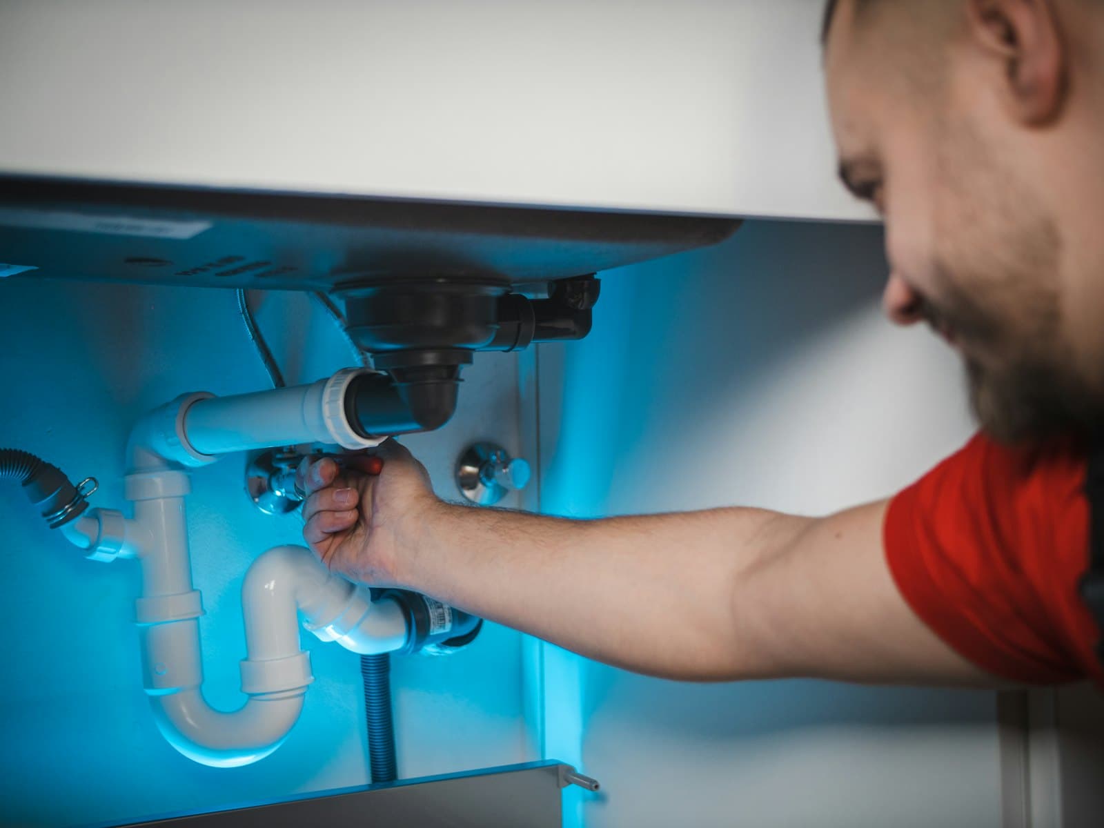 A plumber tightening a valve under a sink