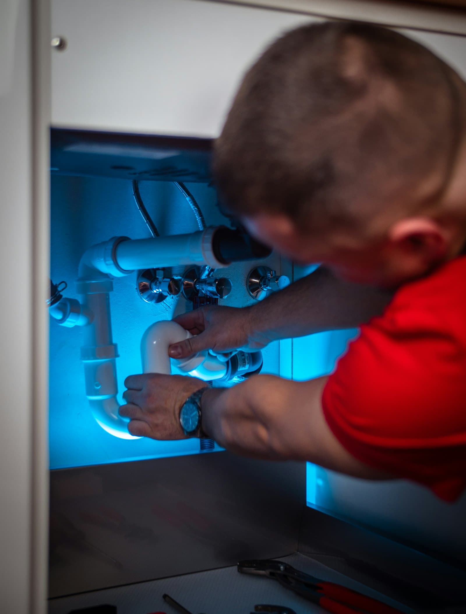 A plumber fitting a waste trap under a sink